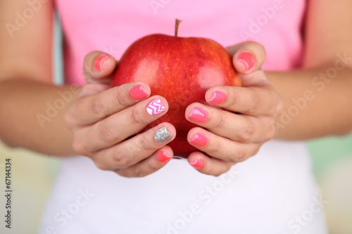 Female hand with stylish colorful nails holding red apple 