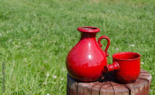 ceramic red water jug and cup on stump on nature