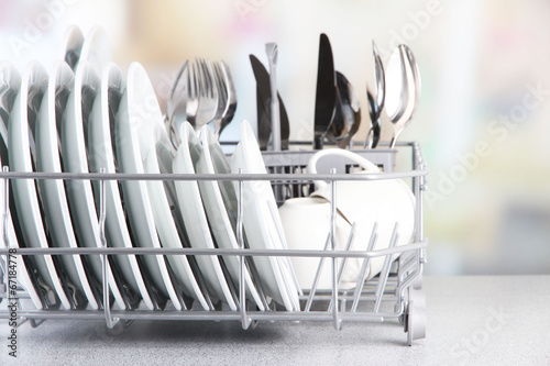 Clean dishes drying on metal dish rack on light background photo