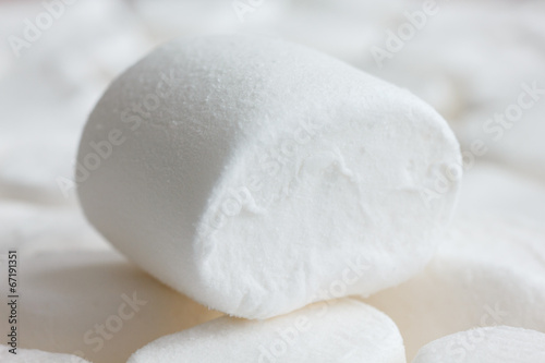 One white marshmallow on other marshmallows. Blurry background.