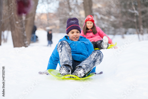 boy and girl sliding on sledges in park.