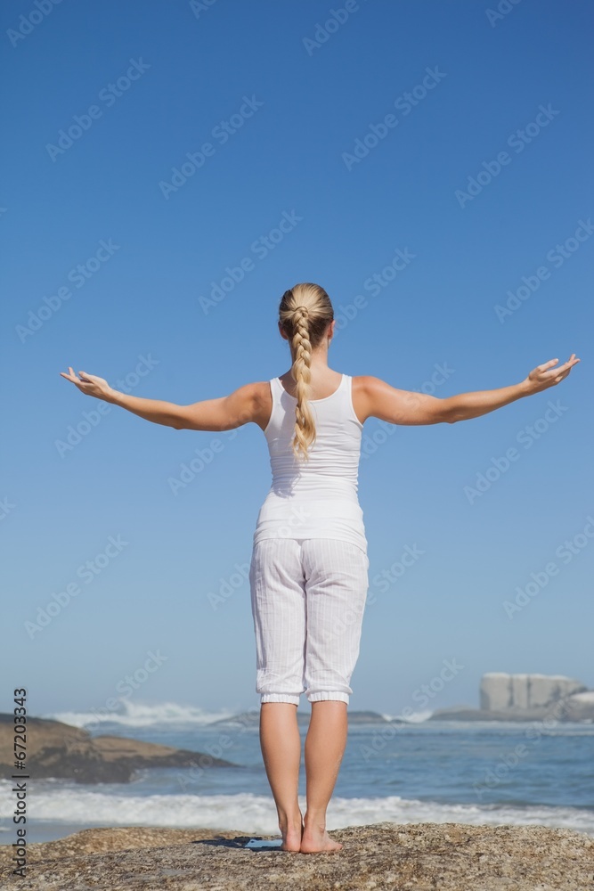 Blonde woman standing on beach on rock