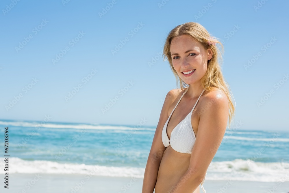 Beautiful blonde in white bikini smiling at camera on the beach