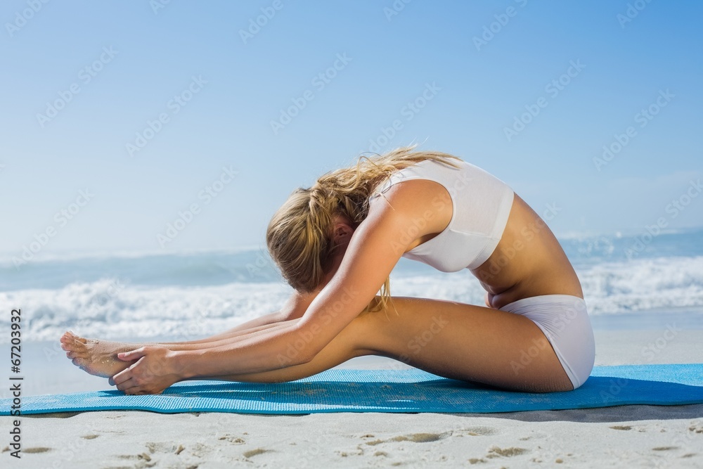 Gorgeous fit blonde in seated forward bend pose on the beach Gorgeous fit blonde in seated forward bend pose on the beach