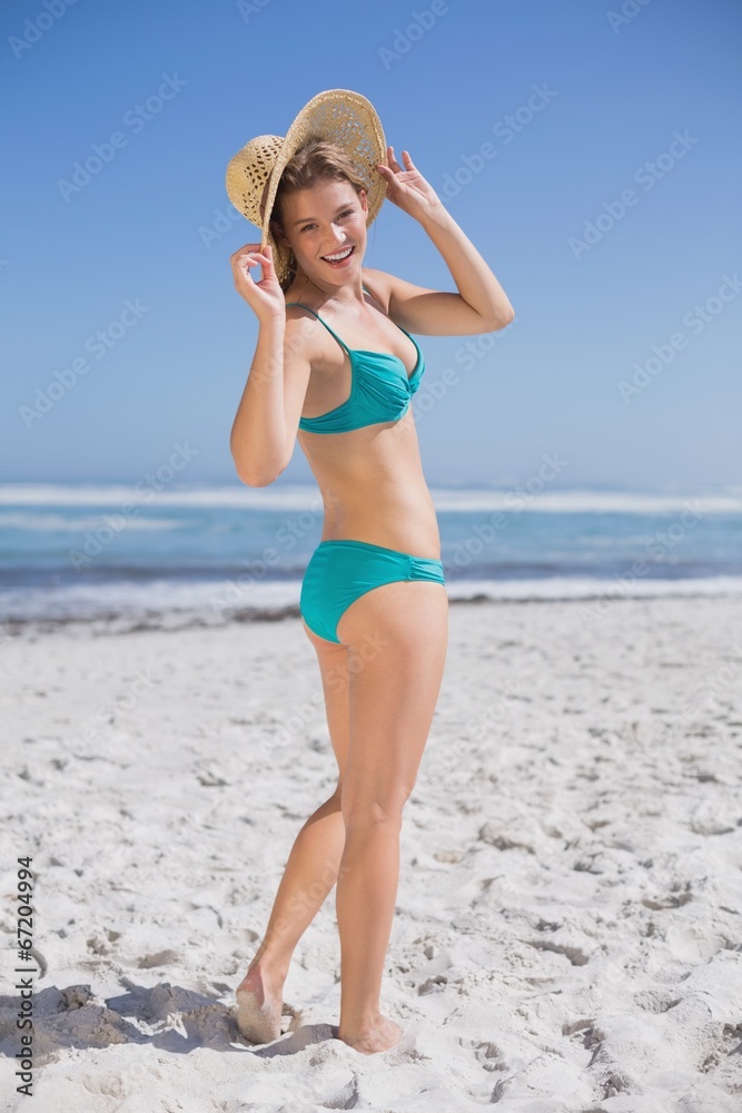 Slender woman in bikini on beach wearing sunhat smiling at camer Slender woman in bikini on beach wearing sunhat smiling at camer