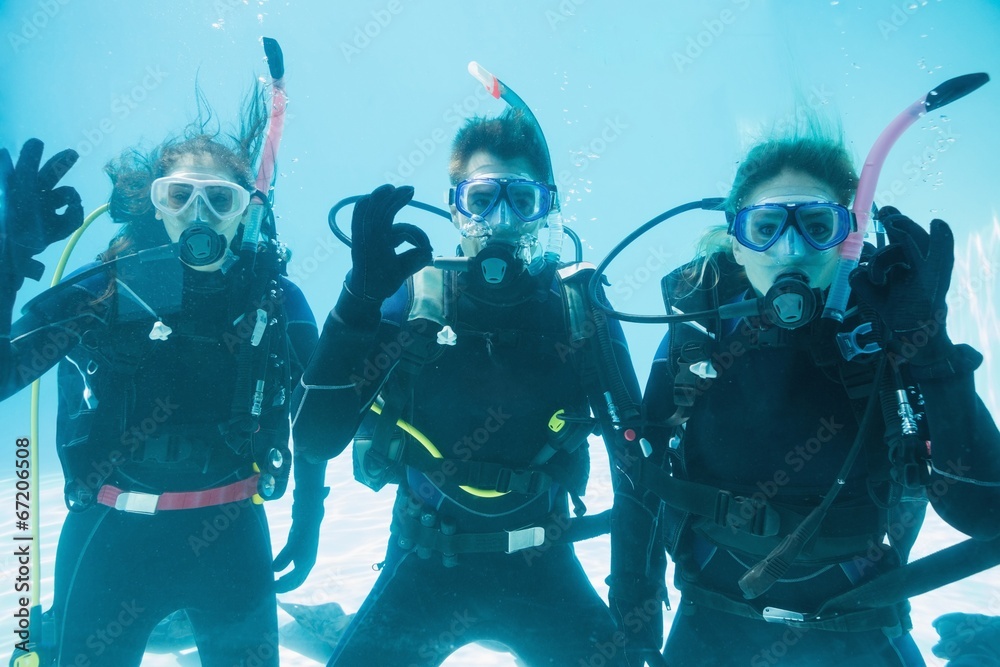 Friends on scuba training submerged in swimming pool looking to Friends on scuba training submerged in swimming pool looking to