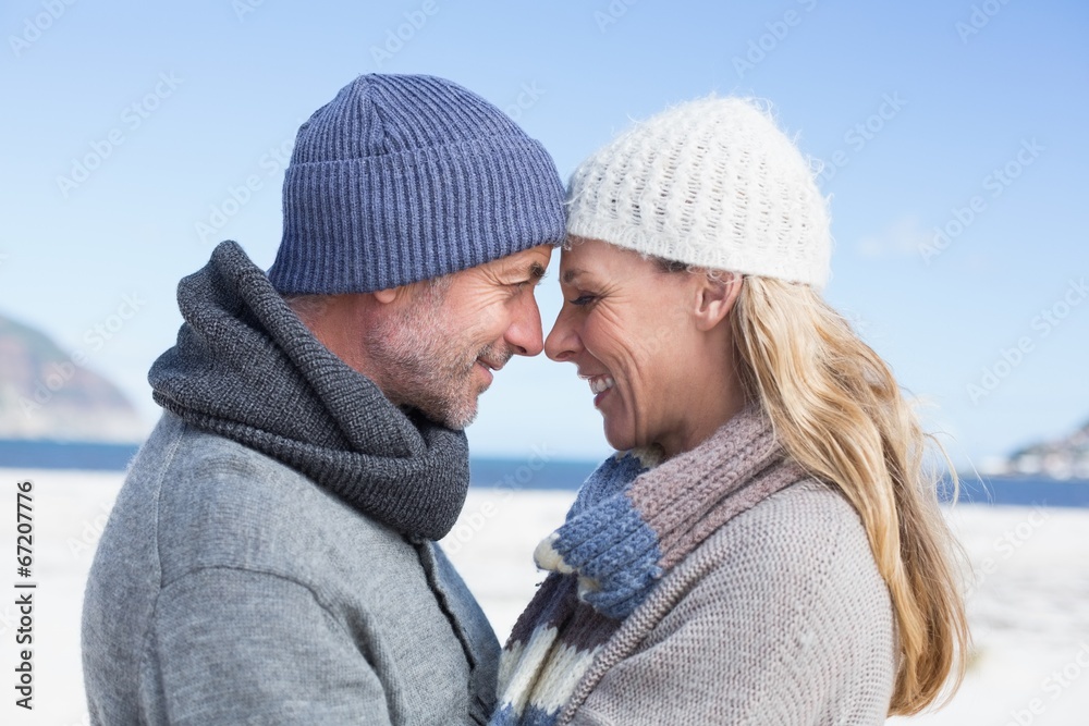 Attractive couple smiling at each other on the beach in warm clo Attractive couple smiling at each other on the beach in warm clo