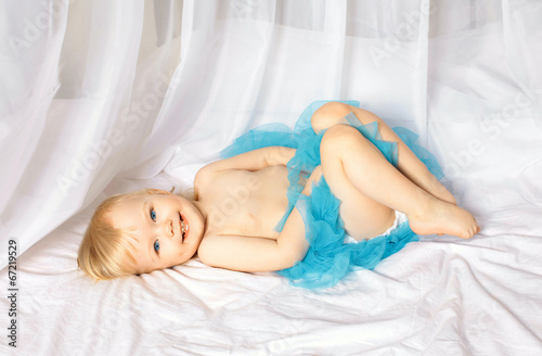 Little cute smiling baby girl lying on a bed in a blue skirt