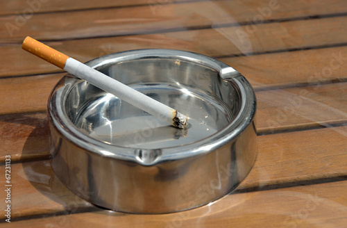 Metal ashtray with a cigarette on a wooden table
