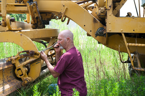 Man using pliers to work on blade of roadgrader