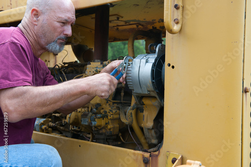 Man using pliars to install new alternator on roadgrader