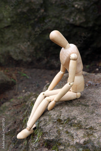 Wooden pose puppet sitting on stone, outdoors