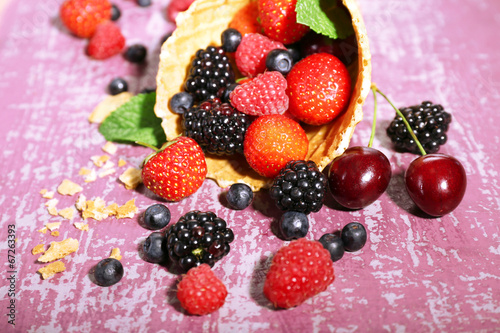 Different ripe berries in sugar cone  on purple background