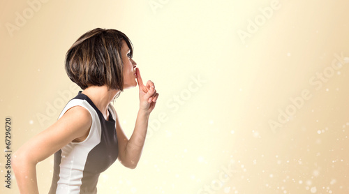 Woman doing silence gesture over ocher background