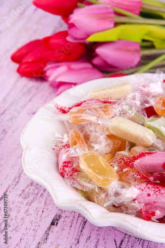 Tasty candies in bowl with flowers on wooden background