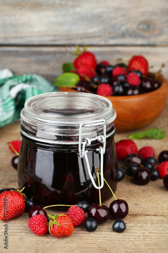 Quadro su tela Tasty jam with berries in glass jar on wooden table