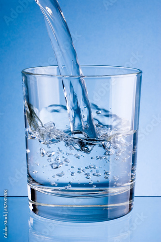 Pouring water into glass on a blue background