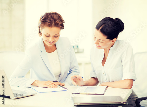 two smiling businesswomen working in office © Syda Productions