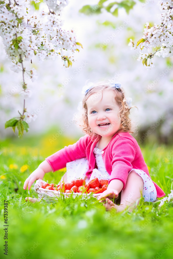 Nice toddler girl eating strawberry in blooming garden