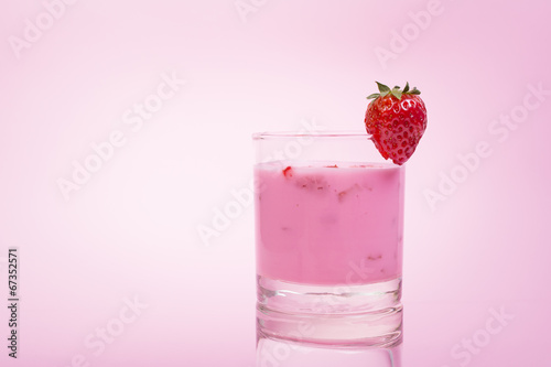 Fresh strawberry smoothie in a glass against pink background