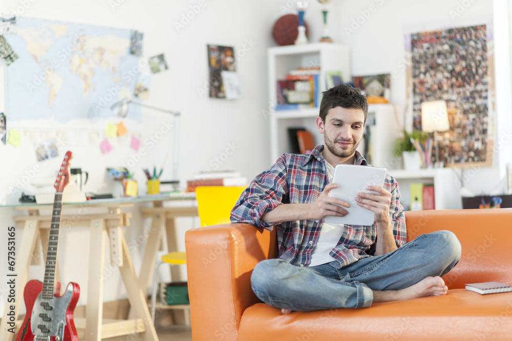 Obraz premium young student sits on a sofa is using a digital tablet at home