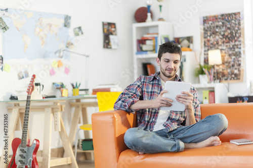 Canvas Print young student sits on a sofa is using a digital tablet at home