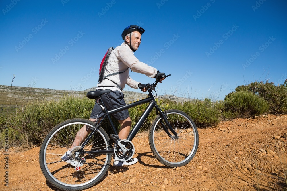 Fit cyclist pushing bike uphill on country terrain