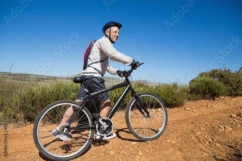 Fit cyclist pushing bike uphill on country terrain