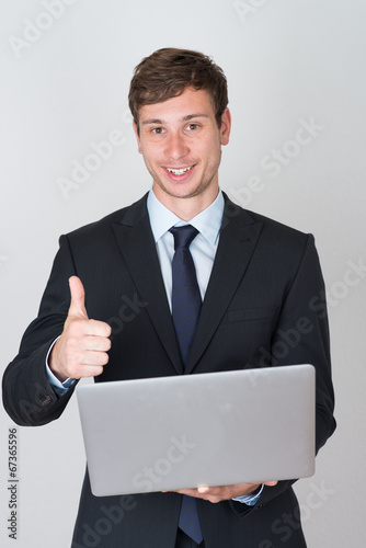 handsome businessman holding a laptop shows thumb up