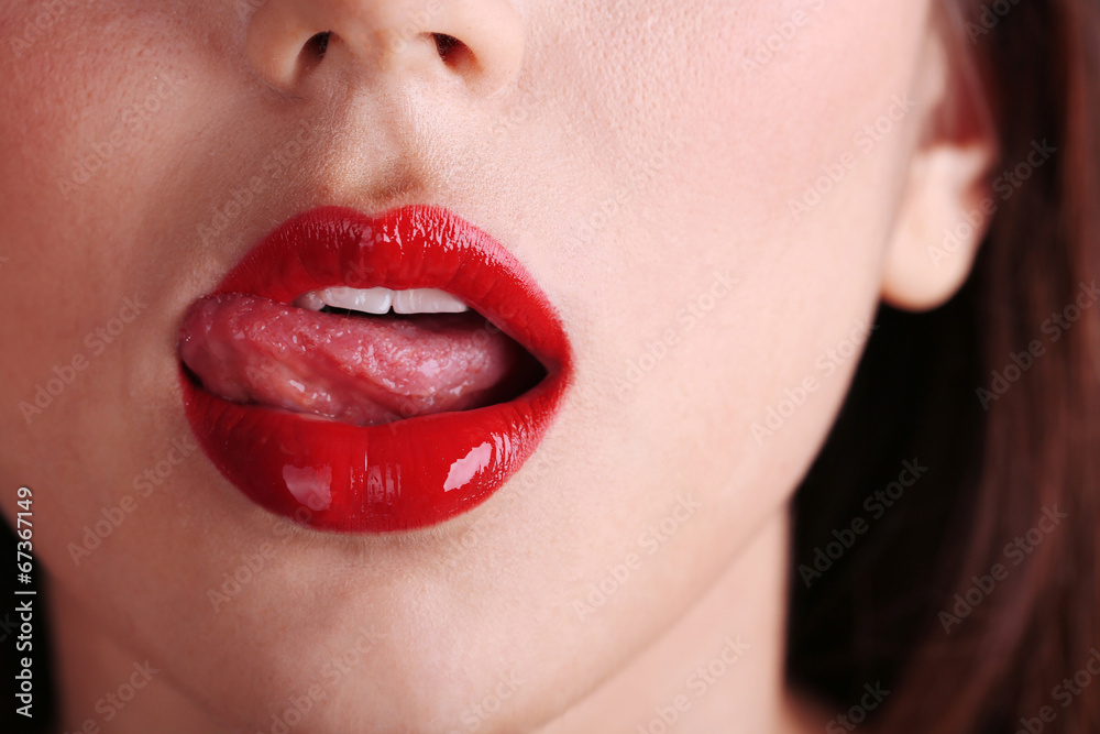 Naklejka premium Girl licks red lips on dark background