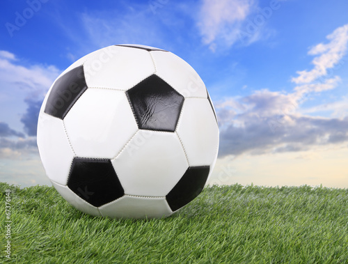 Stitch leather soccer ball on green field blur sky.