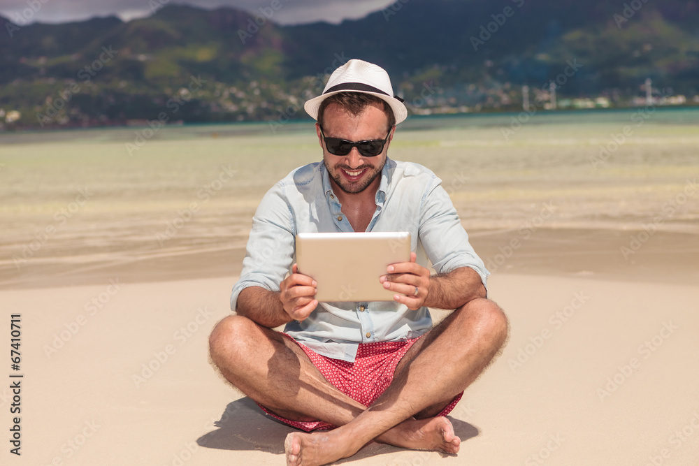 smiling man reading on  tablet  while sitting down the beach