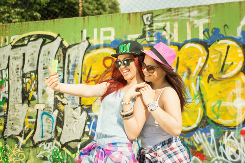 Two young girl friends taking a selfie against graffiti wall