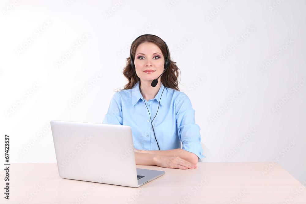 Young woman with headset sitting at table with notebook in room Young woman with headset sitting at table with notebook in room