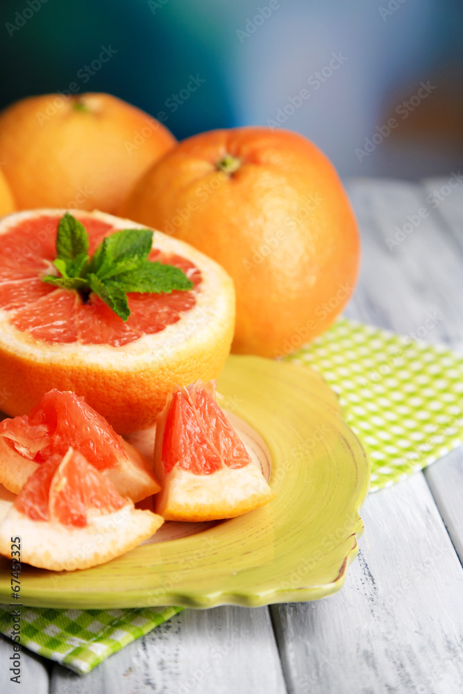 Ripe grapefruits on plate on color wooden background