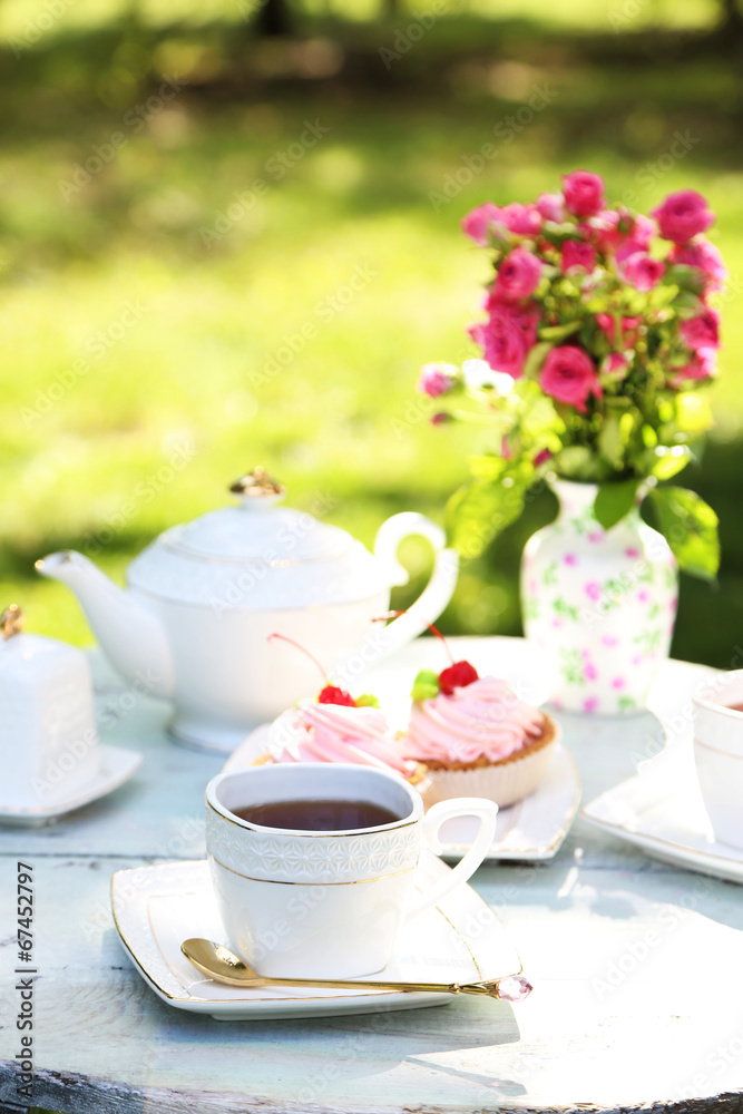 Coffee table with teacups and tasty cakes in garden Coffee table with teacups and tasty cakes in garden