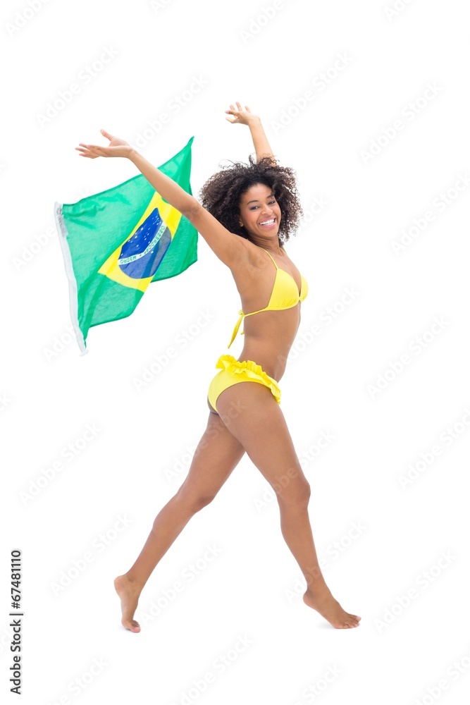 Fit girl in yellow bikini holding brazil flag smiling at camera Fit girl in yellow bikini holding brazil flag smiling at camera