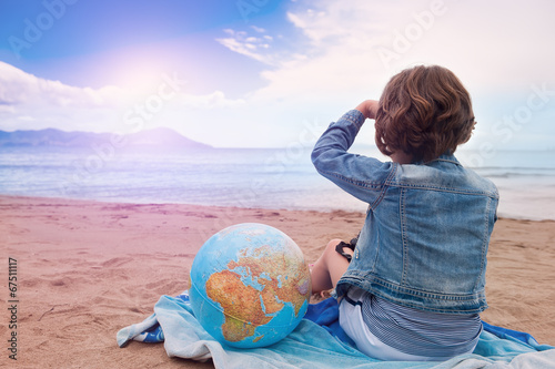 Young Girl with globe on the beach looking at the sunset on sea