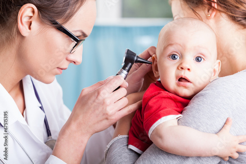 Doctor examining baby boy with otoscope photo