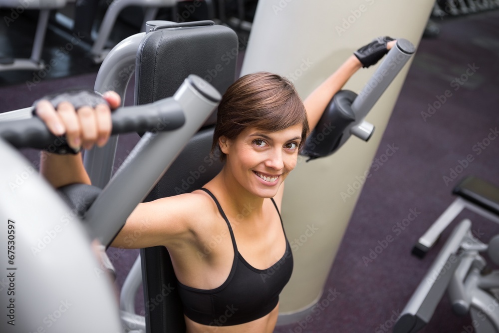 Fototapeta premium Smiling brunette using weights machine for arms