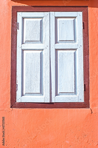 decorative white window on an old orange stucco wall © kannapon