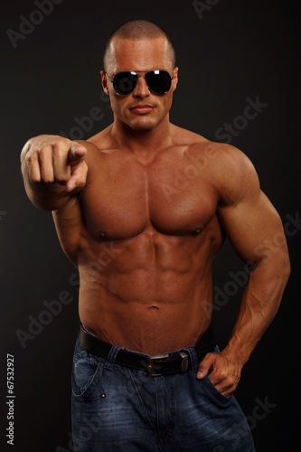 Handsome muscular man shows on you on dark background