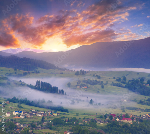Colorful summer sunrise in the foggy mountain village.