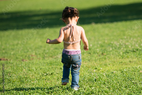 Happy little toddler girl walking on the green grass