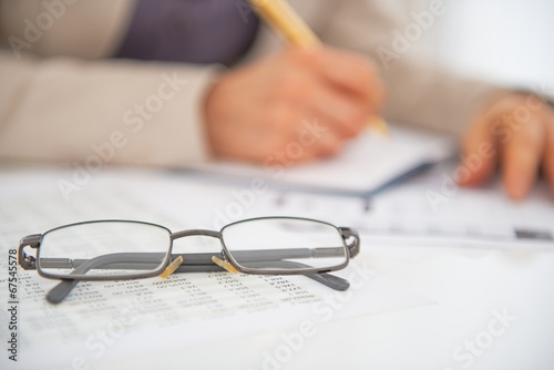 Closeup on eyeglasses on table and woman working in background