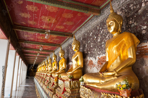 golden buddhas lined up along the wall in temple