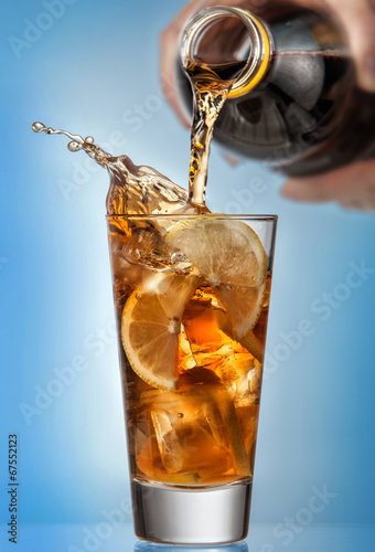 Glass of splashing iced tea with lemon on blue background