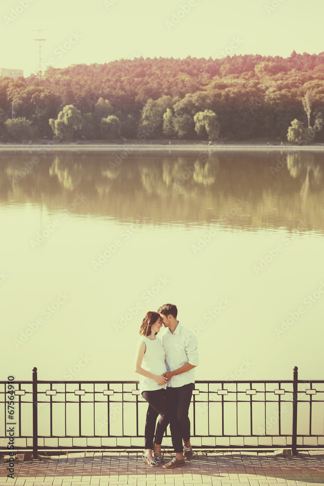 Happy and young pregnant couple hugging in nature at the lake. V