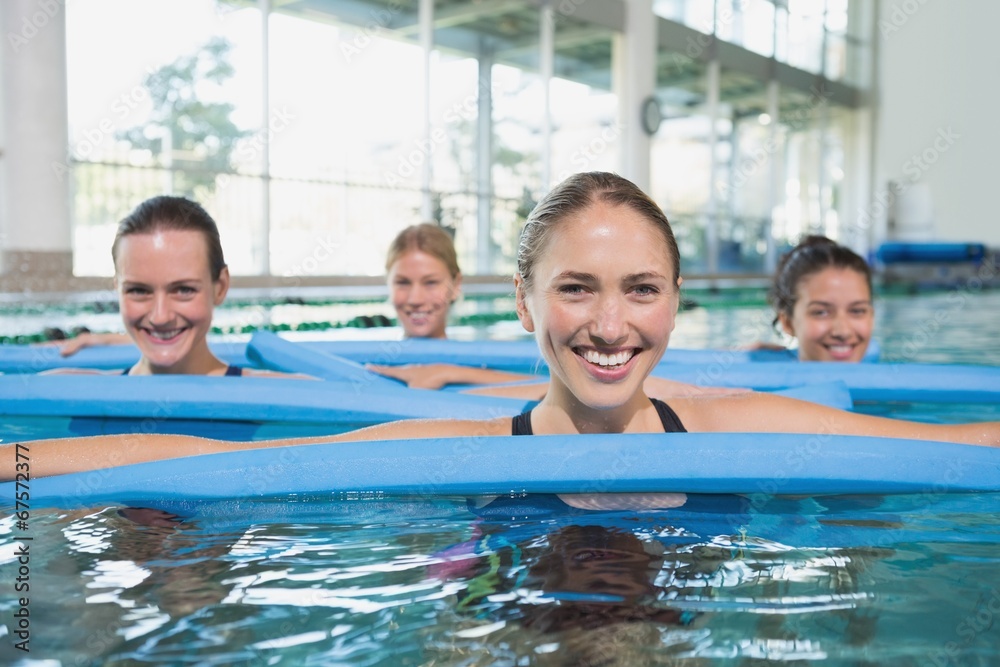 Female fitness class doing aqua aerobics with foam rollers Female fitness class doing aqua aerobics with foam rollers