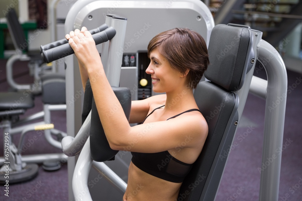 Fototapeta premium Happy brunette using weights machine for arms